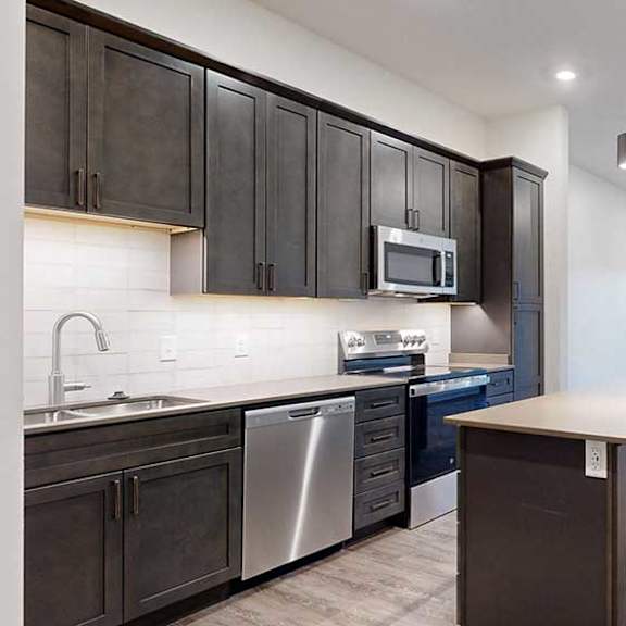 Thumbnail 3 of 25 a kitchen with dark brown cabinets and a stainless steel dishwasher and microwave in front of a living room