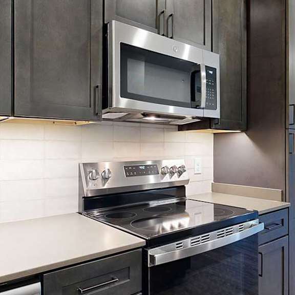 Thumbnail 5 of 25 a kitchen with dark wooden cabinets, tile backsplash, quartz countertops, and a stainless steel microwave and oven