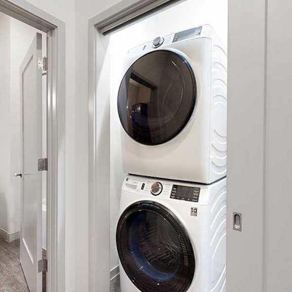 Thumbnail 24 of 25 a white stackable washing machine and dryer in a laundry room next to a bathroom