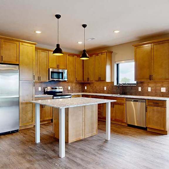 Thumbnail 16 of 33 A kitchen with warm wooden cabinets, quartz countertops, a central island, and stainless steel appliances.