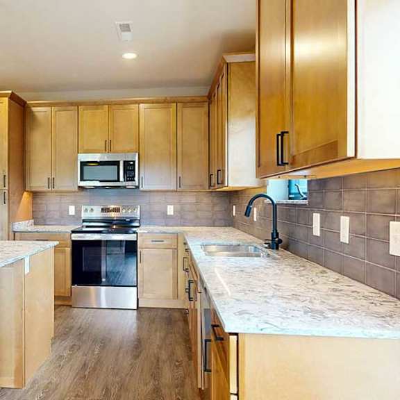 Thumbnail 21 of 33 A kitchen with warm wooden cabinets, quartz countertops, a central island, and stainless steel appliances.