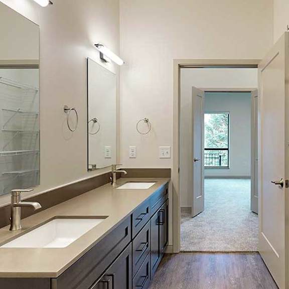 Thumbnail 30 of 33 a bathroom with a double sink, mirror, and a door leading to a walk-through closet