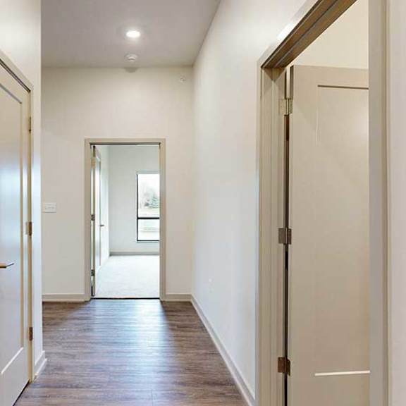 Thumbnail 3 of 33 a hallway with an open door on the right, a closet double door on the left, and a bedroom at the end of the hall