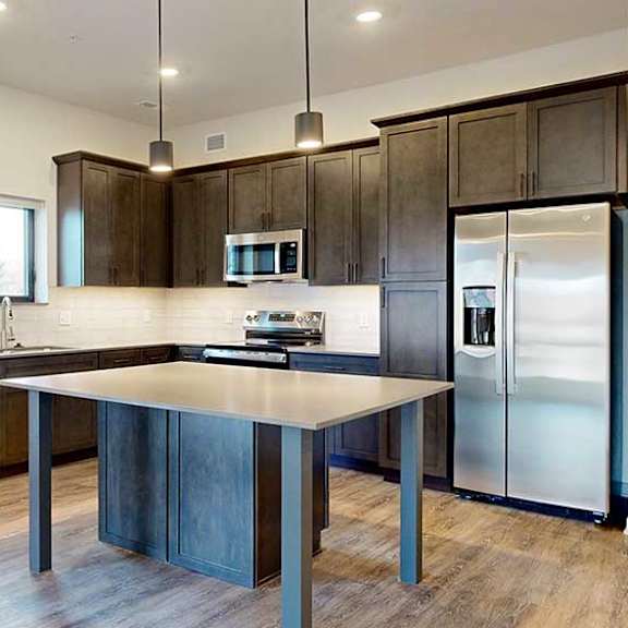 Thumbnail 14 of 33 a modern L-shaped kitchen with dark cabinets, stainless steel appliances, quartz counter tops, and a central island table