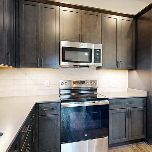 Thumbnail 15 of 33 a kitchen with dark wooden cabinets, stainless steel appliances, tile backsplash, and quartz countertops
