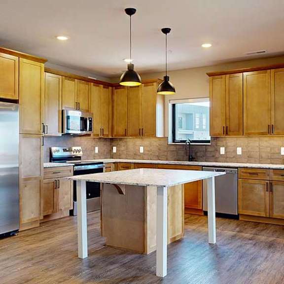 Thumbnail 18 of 33 a kitchen with light brown wooden cabinets, stainless steel appliances, a tile backsplash, a large central island, and quartz countertops
