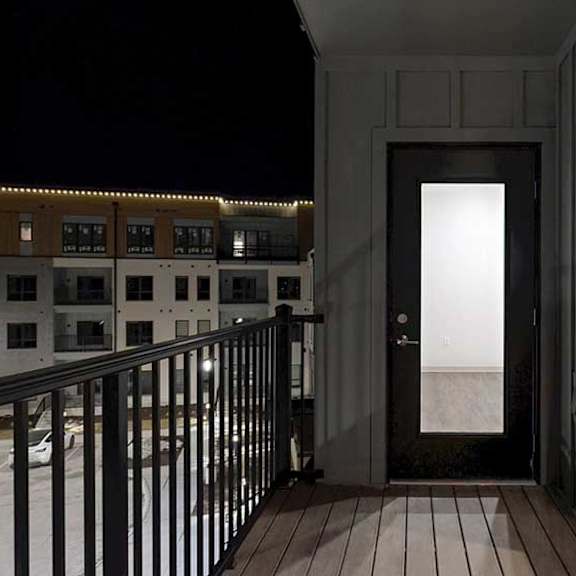 Thumbnail 14 of 25 a balcony at night with a windowed door to the living room and a large window to the bedroom