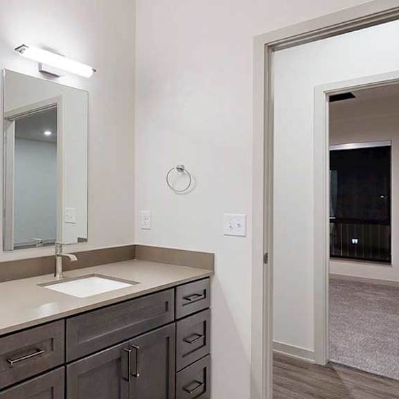 Thumbnail 25 of 25 a bathroom with a quartz countertop vanity sink featuring dark wood cabinets, a slim mirror, and overhead lighting