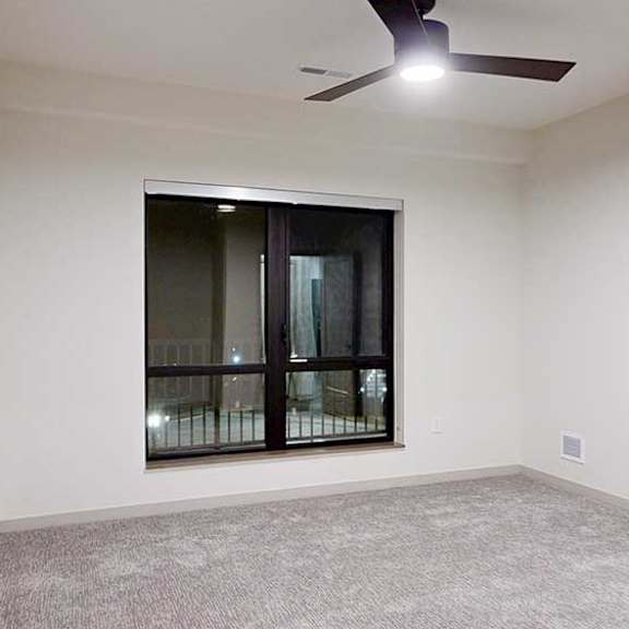 Thumbnail 18 of 25 a bedroom with white walls, a large window, a ceiling fan, and carpeted flooring