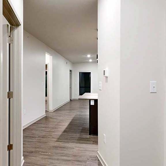 Thumbnail 2 of 25 a hallway with closed closets on either side leading to an open kitchen and living room area