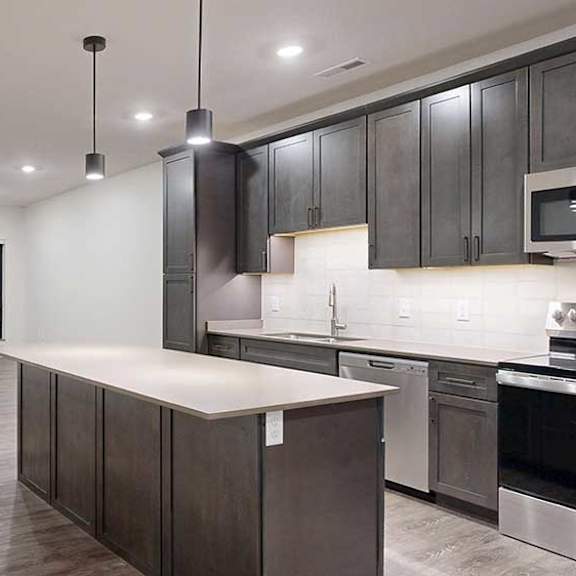 Thumbnail 4 of 25 a modern kitchen with dark cabinets next to a long living room with two windows