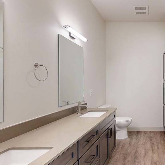 Thumbnail 48 of 50 Apartment bathroom with a double-sink vanity, wood-style flooring, and bright lighting.