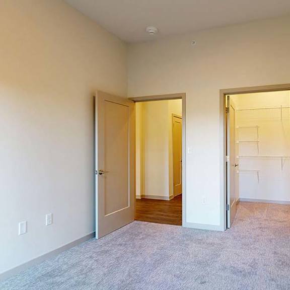 Thumbnail 43 of 50 Bright apartment bedroom with neutral carpet, open doorway, and walk-in closet.