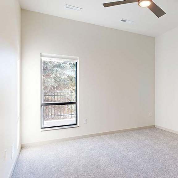 Thumbnail 42 of 50 Bright, empty apartment bedroom with neutral carpet, white walls, a vaulted ceiling, and a large window providing natural light.