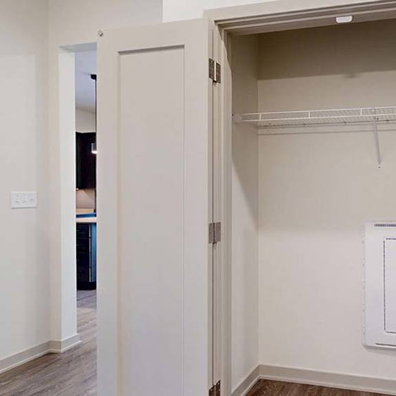 Thumbnail 38 of 50 Apartment laundry closet with bifold doors, upper wire shelf, washer and dryer hookups, and hard-surface flooring at the entry.