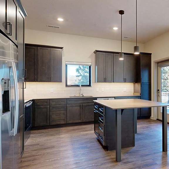 Thumbnail 35 of 50 Open apartment kitchen with dark cabinets, island, stainless steel appliances, and wood-style flooring.