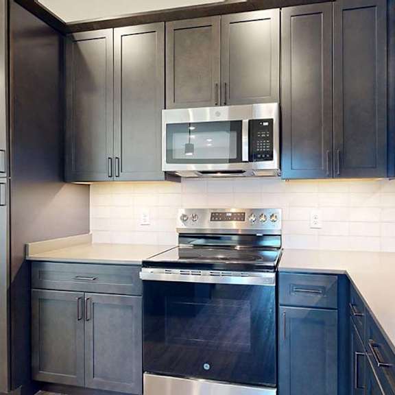Thumbnail 37 of 50 Apartment kitchen with dark cabinets, stainless steel oven and microwave, and light backsplash.