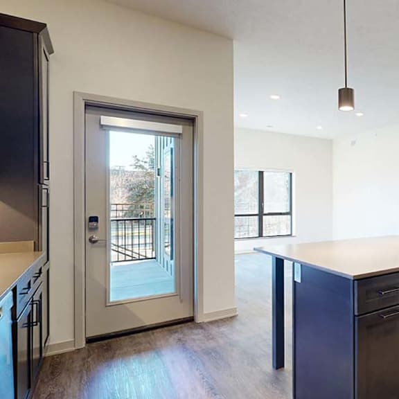 Thumbnail 34 of 50 Open apartment living area with kitchen island, pendant lighting, wood-style flooring, and patio door.