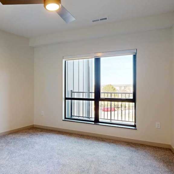 Thumbnail 16 of 21 A bedroom with a large floor-to-ceiling window, a ceiling fan, and carpeted flooring.