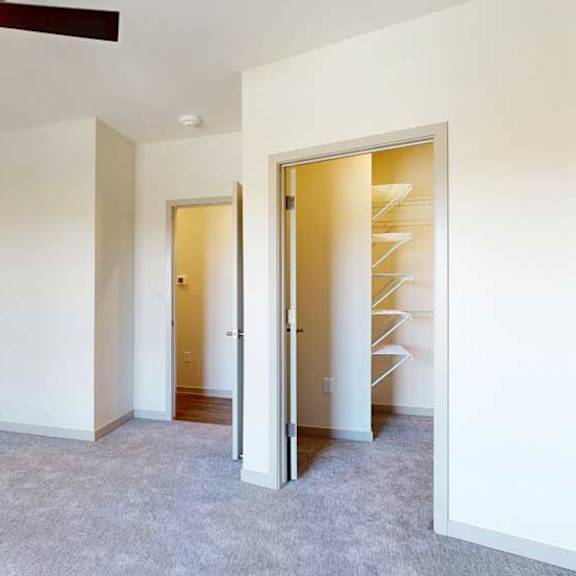 Thumbnail 17 of 21 A carpeted bedroom with a walk-in closet, ceiling fan, and a door open to the living room.