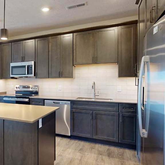 Thumbnail 3 of 21 A kitchen with dark wooden cabinets, quartz countertops, an island, and stainless steel appliances.