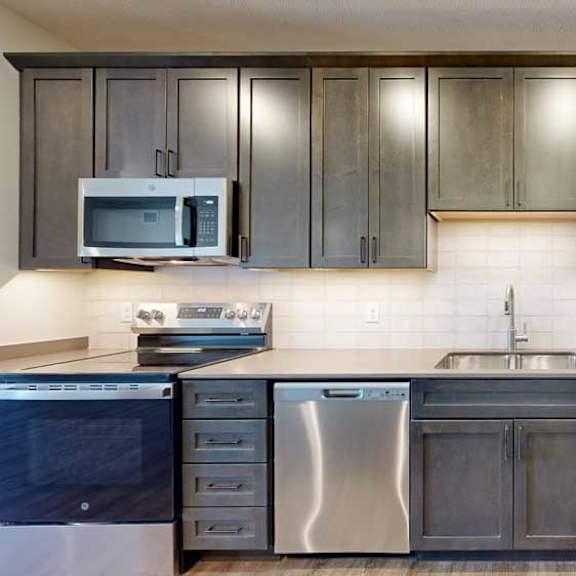 Thumbnail 5 of 21 A modern kitchen sink with quartz counters, dark wooden cabinets, and a tile backsplash.