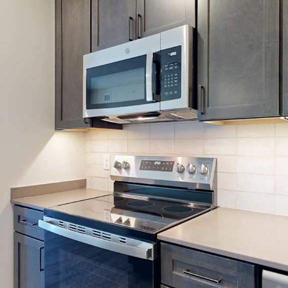 Thumbnail 6 of 21 A close up of the stainless steel microwave and range in a kitchen with dark wooden cabinets.