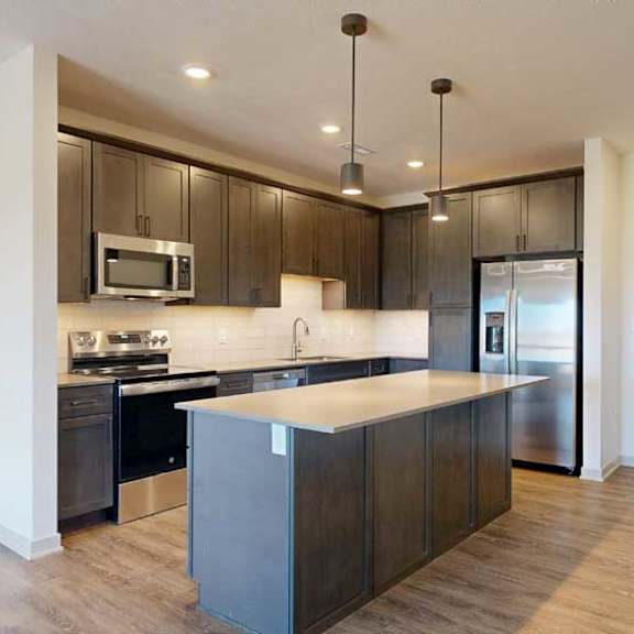 Thumbnail 4 of 21 A kitchen with dark wooden cabinets, quartz countertops, an island, and stainless steel appliances.