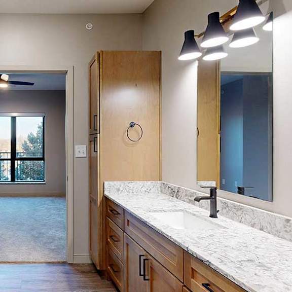 Thumbnail 22 of 26 a bathroom with tan wooden cabinets, quartz countertops, a tall storage cabinet, and a door to the bedroom