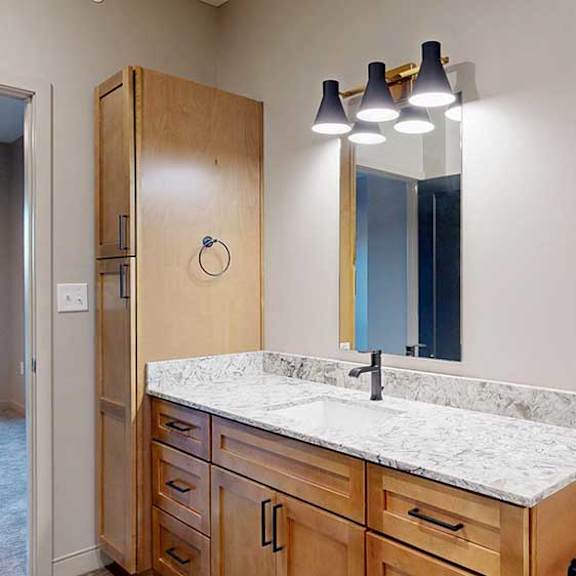 Thumbnail 21 of 26 a bathroom with tan cabinets, a quartz vanity sink, and a tall storage cabinet