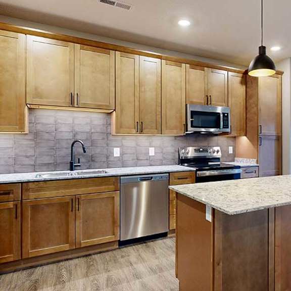 Thumbnail 3 of 26 a kitchen with tan wooden cabinets, a large central island, quartz countertops, tile backsplash, and stainless steel appliances