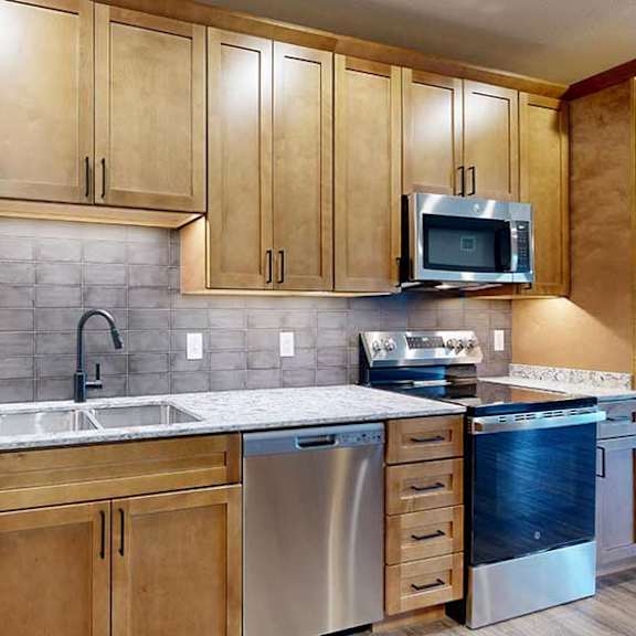 Thumbnail 6 of 26 a kitchen with tan wooden cabinets, a tile backsplash, quartz countertops, and stainless steel appliances