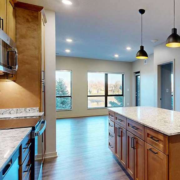 Thumbnail 5 of 26 a large kitchen island with tan cabinets and quartz countertop in front of an open living room with large windows