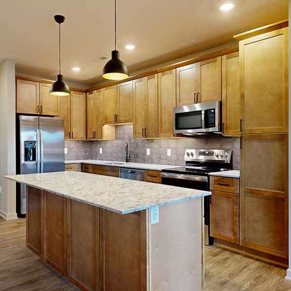 Thumbnail 8 of 26 a kitchen with tan wooden cabinets, a large central island, quartz countertops, tile backsplash, and stainless steel appliances