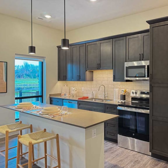 Thumbnail 2 of 20 a kitchen with dark cabinets, a tile backsplash, quartz countertops, stainless steel appliances, and a micro-island
