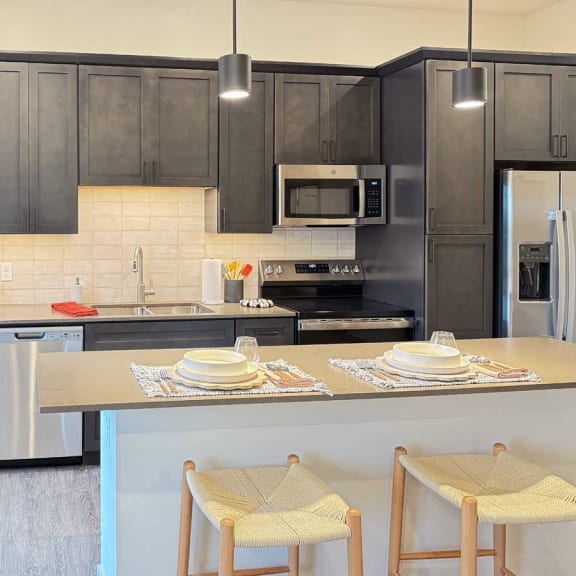 Thumbnail 4 of 20 a kitchen with dark cabinets, quartz countertops, stainless steel appliances, and a center micro-island with two stools
