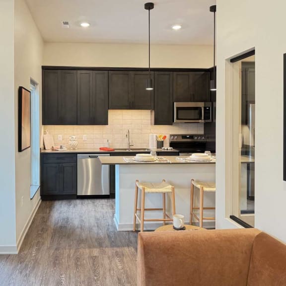 Thumbnail 10 of 20 a modern kitchen with dark cabinets, stainless steel appliances, and a micro-island next to a door out to a patio walk-out