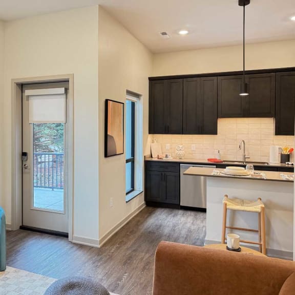 Thumbnail 11 of 20 a modern living room with a door to a walk-out patio next to a kitchen with dark cabinets