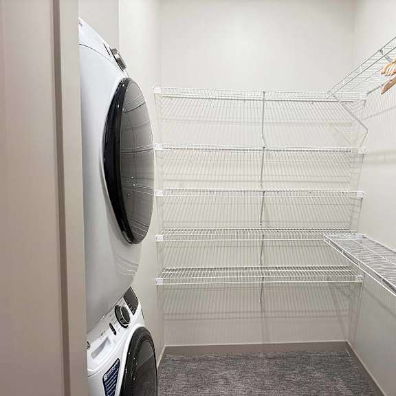 Thumbnail 17 of 20 a walk-in closet with built-in shelving and hanging space and a stackable washer and dryer in it