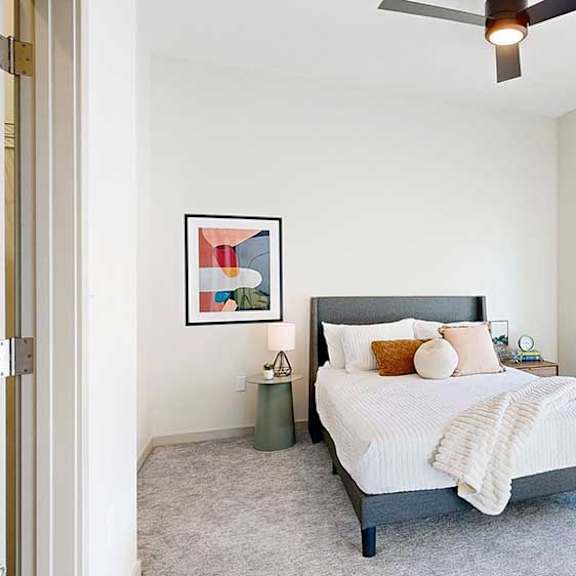 Thumbnail 14 of 23 A furnished bedroom with a bed, modern art, a ceiling fan, and a floor-to-ceiling window.