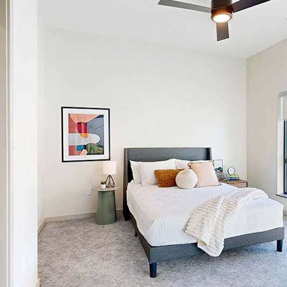 Thumbnail 17 of 26 a view of the bedroom from the doorway, furnished with modern decor, a ceiling fan, and a large window overlooking the courtyard