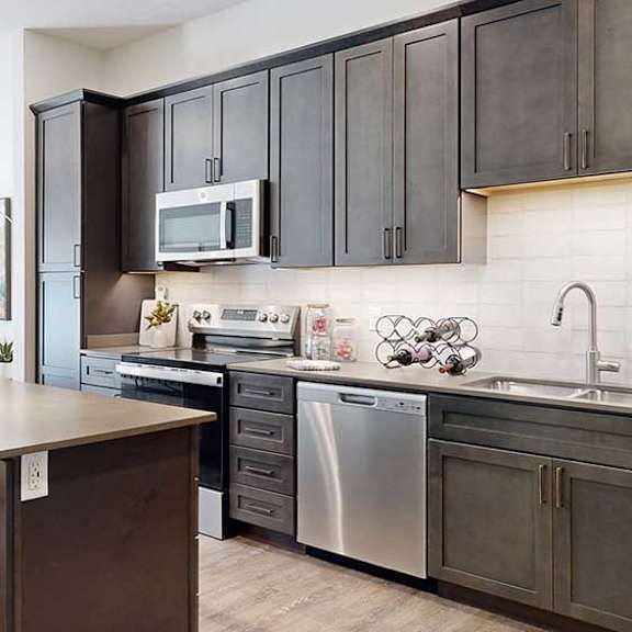 Thumbnail 5 of 26 a modern kitchen with a stainless steel appliances, quartz countertops, a light tile backsplash, dark wooden cabinets, and a large central island