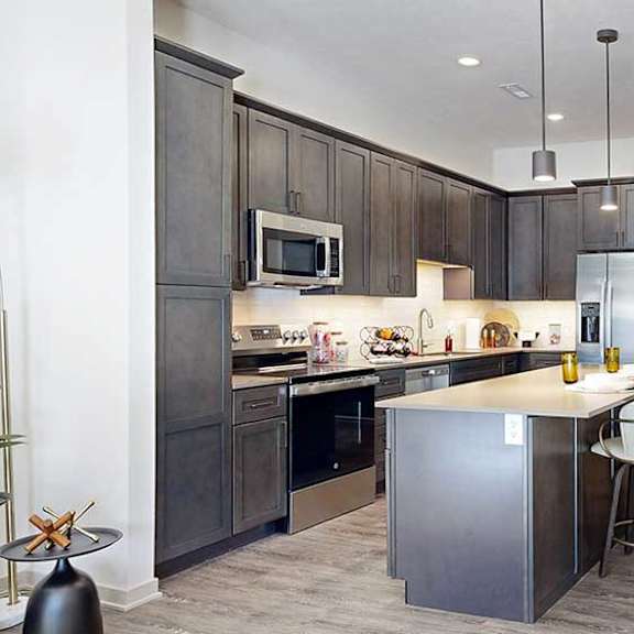 Thumbnail 7 of 23 A kitchen with dark wooden cabinets, quartz countertops, an island, and stainless steel appliances.