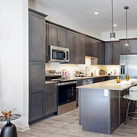 Thumbnail 2 of 26 a modern kitchen with a stainless steel appliances, quartz countertops, a light tile backsplash, dark wooden cabinets, and a large central island