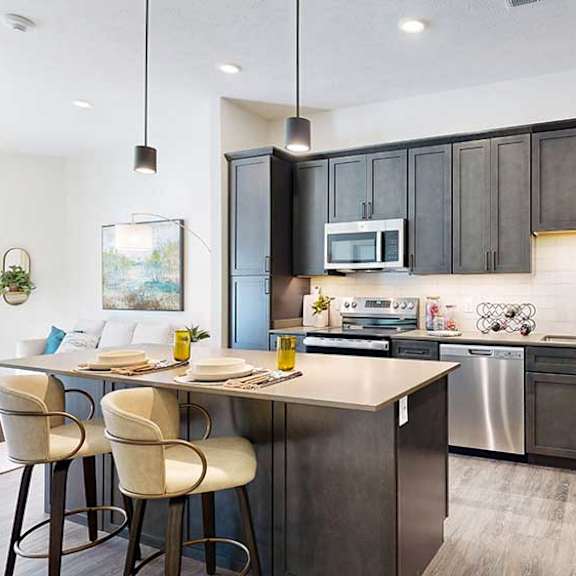 Thumbnail 3 of 23 A kitchen with dark wooden cabinets, quartz countertops, an island, and stainless steel appliances.