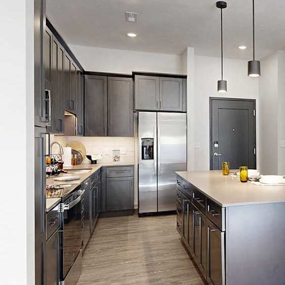 Thumbnail 6 of 23 A kitchen with dark wooden cabinets, quartz countertops, an island, and stainless steel appliances.
