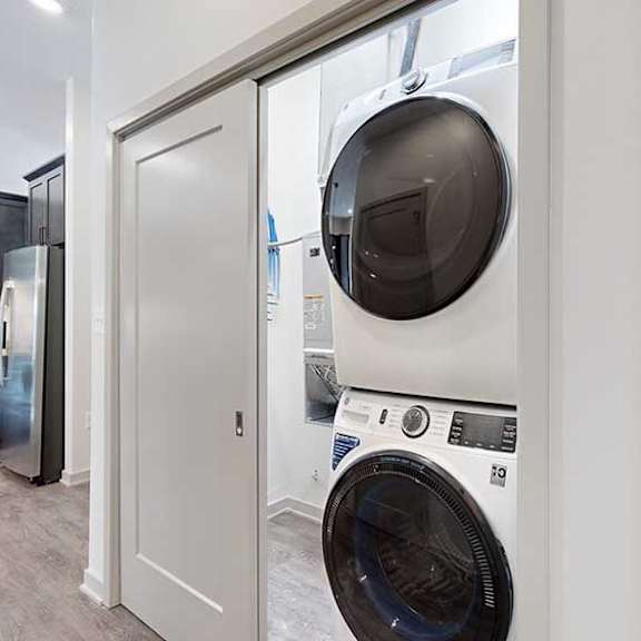 Thumbnail 25 of 26 a white and black stackable full-size washer and dryer in a double door closet in the front hallway