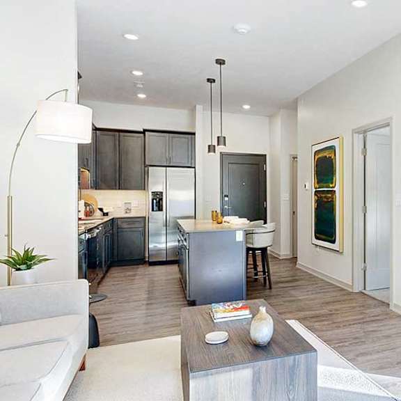 Thumbnail 13 of 23 A living room with hardwood-style flooring and kitchen with dark wooden cabinets.