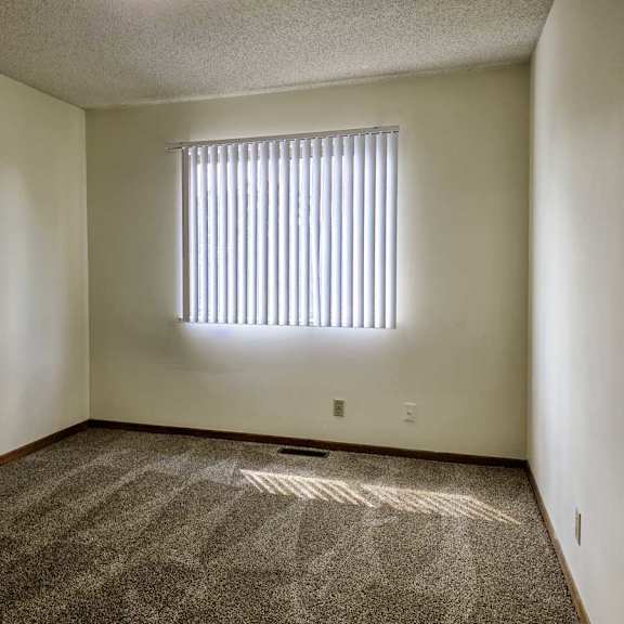 Thumbnail 10 of 11 A carpeted bedroom with a window with blinds.
