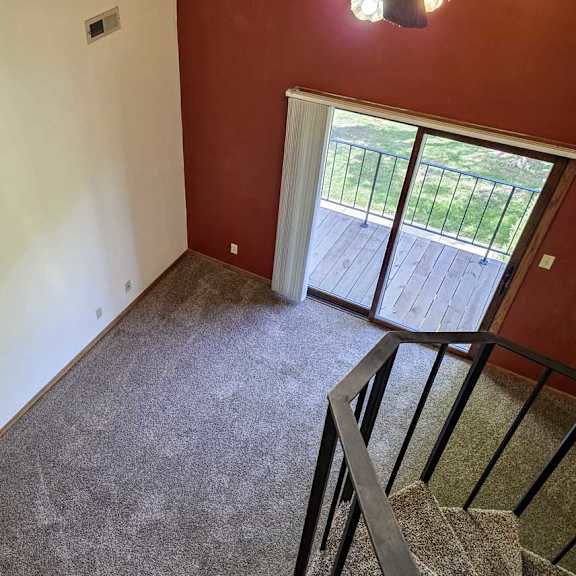 Thumbnail 7 of 11 A view of a living room with a red accent wall and a sliding glass door to a balcony, from a loft area.